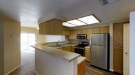 This single-story residence is thoughtfully designed to maximize functionality and comfort. The kitchen serves as a central feature of the home, showcasing warm honey-toned wood cabinetry that extends to the ceiling, offering generous storage throughout. A suite of stainless steel appliances — including a refrigerator, electric range, and over-the-range microwave — equips the space for everyday use. An L-shaped countertop layout provides ample workspace, while a built-in sink with a standard faucet adds practicality. A flush-mounted panel light fixture overhead ensures the kitchen is well-lit.

A wraparound breakfast bar extends from the kitchen, creating a natural boundary between the cooking area and the adjoining living space. This open-concept layout promotes a sense of flow and connectivity throughout the home. The living areas feature wall-to-wall carpeting, lending a soft, comfortable feel underfoot.

A hallway off the main living area leads to additional rooms, including a bathroom with wood-toned vanity cabinetry. A textured ceiling is consistent throughout the space, and neutral wall tones contribute to a clean, understated aesthetic.