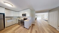 Located at Renaissance Bay Residences in Patchogue, New York, this thoughtfully updated single-floor home offers a clean, contemporary aesthetic throughout. The open-concept kitchen is a standout feature, outfitted with crisp white shaker cabinetry, light granite countertops, a full suite of stainless steel appliances, and light hardwood flooring that flows seamlessly into the adjacent living and dining areas. A dedicated dining nook provides an intimate space for meals, with a window overlooking lush greenery. The spacious living room is bright and airy, featuring recessed lighting, sliding glass doors that invite natural light and outdoor access, and a neutral color palette that creates a welcoming ambiance. The bedroom offers plush carpeting, a ceiling fan, a closet with built-in shelving, and a window that brings in natural light. The bathroom is elegantly finished with large-format beige wall tiles surrounding a deep soaking tub, a marble-topped vanity, and polished chrome fixtures. Consistent hardwood flooring throughout the main living areas ties the home together, while neutral wall tones complement the modern finishes. The overall design is clean, functional, and move-in ready.