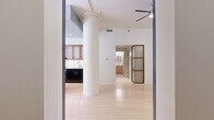 This well-appointed one-bedroom, two-bathroom residence offers a generously sized single-floor layout with a clean, modern aesthetic throughout. Light hardwood flooring flows seamlessly across the open-plan living and kitchen area, creating a bright and cohesive atmosphere. A striking structural column serves as an architectural focal point in the main living space, which is bathed in natural light from large windows and glass French doors that open to city views of surrounding buildings.

The kitchen is thoughtfully designed with dark lower cabinetry contrasted by warm wood upper cabinets with frosted glass inserts, granite countertops, a white tile backsplash, stainless steel appliances including a range and French door refrigerator, and an undermount sink — delivering both style and functionality.

The bedroom is a comfortable, well-proportioned retreat with light hardwood floors, white walls, and closet access. Two closets serve the unit, providing ample storage throughout.

Both bathrooms are finished with warm wood vanities, white countertops, framed mirrors, and built-in shelving. One bathroom features a glass-enclosed walk-in shower with full white tile surround and dual showerheads. A dedicated laundry room houses a stacked Whirlpool washer and dryer alongside an in-unit water heater, adding everyday convenience to this thoughtfully laid-out urban residence.
