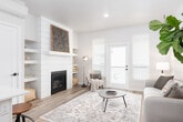 This thoughtfully designed three-story residence offers a functional and comfortable layout across its multiple levels, connected by a carpeted staircase with a sleek white handrail. The main living area centers around a striking shiplap fireplace with a white mantel, complemented by light hardwood-style flooring and a glass door leading to a balcony, filling the space with natural light. Adjacent to the living area, the dining room features a modern chandelier and a large window framing outdoor views, creating a bright and inviting setting for gatherings.

The kitchen is outfitted with white shaker cabinetry, subway tile backsplash, and stainless steel appliances including a French door refrigerator, gas range, and over-the-range microwave. A dedicated office on the entry level provides a practical workspace with natural light and hardwood-style flooring. The bedrooms are carpeted and well-proportioned; one includes a walk-in closet, while another features a wall-mounted mini-split unit and a large window with neighborhood views. Bathrooms are clean and functional, featuring tub-shower combinations, white vanities, and ample mirror space throughout.