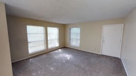 This single-story unit in Sherman offers a practical and functional layout spread across multiple rooms. The main living area is generously sized, featuring wall-to-wall carpeting, neutral beige walls, and a textured popcorn ceiling. Multiple windows flood the space with natural light, and a sliding glass door opens to a balcony overlooking mature trees, creating a pleasant indoor-outdoor connection.

The living space extends into a secondary area, also carpeted, providing flexibility for dining or additional seating arrangements. From this area, sightlines connect to a kitchen visible in the background, suggesting an open, flowing layout between common spaces.

The bedroom is well-proportioned, featuring carpet flooring, two windows that bring in natural light, and a notable dual-closet configuration along one wall, offering ample storage capacity. The textured ceiling and neutral color palette carry throughout the room, maintaining a consistent aesthetic.

The bathroom is equipped with wood-look vinyl flooring, a full-sized tub and shower combination with a white surround, a toilet, and a vanity with a countertop. A textured ceiling completes the space.

Overall, the unit maintains a consistent neutral color scheme throughout, with carpeted living and sleeping areas, functional storage solutions, and abundant natural light from multiple windows.