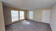 This single-story unit in Sherman offers a practical and functional layout spread across multiple rooms. The main living area is generously sized, featuring wall-to-wall carpeting, neutral beige walls, and a textured popcorn ceiling. Multiple windows flood the space with natural light, and a sliding glass door opens to a balcony overlooking mature trees, creating a pleasant indoor-outdoor connection.

The living space extends into a secondary area, also carpeted, providing flexibility for dining or additional seating arrangements. From this area, sightlines connect to a kitchen visible in the background, suggesting an open, flowing layout between common spaces.

The bedroom is well-proportioned, featuring carpet flooring, two windows that bring in natural light, and a notable dual-closet configuration along one wall, offering ample storage capacity. The textured ceiling and neutral color palette carry throughout the room, maintaining a consistent aesthetic.

The bathroom is equipped with wood-look vinyl flooring, a full-sized tub and shower combination with a white surround, a toilet, and a vanity with a countertop. A textured ceiling completes the space.

Overall, the unit maintains a consistent neutral color scheme throughout, with carpeted living and sleeping areas, functional storage solutions, and abundant natural light from multiple windows.