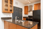 Located at 3217 Pleasant Garden Rd in Greensboro, NC, this single-floor home offers a well-organized layout with a variety of functional living spaces. The kitchen serves as a central highlight, featuring a peninsula island topped with rich dark granite countertops, an integrated stainless steel sink, warm wood cabinetry with glass-front upper cabinets, a stainless steel range hood, and black appliances including a gas range and refrigerator. Track lighting illuminates the space, which transitions seamlessly between hardwood-style flooring and plush carpeting in the adjoining areas. The bedrooms are generously sized, each finished with neutral carpet and ceiling fans for year-round comfort. One bedroom includes a walk-in closet and a window with outdoor views, while another opens via French doors to an exterior space, allowing natural light to fill the room. The bathrooms are cleanly appointed — one features warm wood cabinetry, a dark granite vanity top, hardwood-style flooring, and a tub-shower combination, while a second bathroom offers a white tub-shower surround with brushed nickel fixtures and wood cabinetry. Throughout, the home maintains a neutral, light-toned palette with white walls and clean finishes, creating a bright and livable atmosphere.