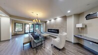 This well-appointed clubroom in Columbia, SC offers a thoughtfully designed, single-floor layout that seamlessly blends functionality with contemporary style. The open-concept main area connects the kitchen and primary living space, creating an inviting environment for gathering and entertainment. Wide-plank hardwood-style flooring runs throughout, lending a cohesive and polished look to the entire space.

The kitchen is equipped with stainless steel appliances, dark espresso cabinetry, granite countertops, and a large island with bar seating. Amber pendant lights hang above the island, adding warmth to the area. A wall-mounted flat-screen TV is positioned nearby, making it ideal for entertaining.

The main living area is anchored by a floor-to-ceiling stone-clad linear fireplace, illuminated by recessed accent lighting. Comfortable seating, a glass-top coffee table, and a statement chandelier contribute to the room's refined ambiance. Large glass doors allow abundant natural light and outdoor views. Colorful abstract artwork adds a vibrant touch to the walls.

A secondary lounge area offers a more intimate setting, featuring a sectional sofa, wall-mounted TV, and carpeted flooring, providing a quieter space for relaxation. Recessed lighting throughout the clubroom ensures consistent, well-distributed illumination across all areas.