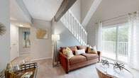 Located at 9804 W 118th St in Overland Park, Kansas, this two-story home offers a thoughtfully designed layout with distinctive architectural character throughout. The living area immediately captures attention with its soaring vaulted ceilings framed by exposed decorative beams and a white-railed staircase. A large sliding glass door floods the space with natural light while providing direct access to a private balcony with outdoor views. A standout brick fireplace with a classic white mantel anchors the living room, adding warmth and visual interest beneath the pitched roofline.

The kitchen features warm wood cabinetry, an extended countertop breakfast bar, a double stainless steel sink, and black appliances, offering a functional and organized cooking space. The bedrooms are generously proportioned with plush carpeting, neutral tones, and ample natural light from well-positioned windows. One upper-level room with a vaulted ceiling serves well as a home office or flexible space.

Bathrooms include vanities with marble-style countertops and wood cabinetry. One bathroom offers a tub-shower combination with wood-look flooring, while another provides an extended vanity with a wide mirror. The overall ambiance is bright, comfortable, and well-suited for everyday living.