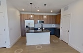 Located at 2380 Staples Rd in San Marcos, TX, this 860-square-foot apartment features 2 bedrooms and 2 bathrooms across a single-floor open-concept layout. Light wood-look flooring runs throughout, complementing the crisp white walls and modern black hardware accents that define the unit's contemporary aesthetic.

The kitchen serves as the centerpiece of the living area, showcasing a large island with dark granite countertops, dual pendant globe lights, and stainless steel appliances including a refrigerator and microwave. Two-tone cabinetry combines warm wood upper cabinets with deep navy-blue lower cabinets, adding a bold, modern touch.

Both bedrooms are bright and airy, each featuring large windows with outdoor views, ceiling fans with integrated lighting, and built-in closets for ample storage. The primary bedroom spans 150 square feet and includes a walk-in closet with shelving.

The primary bathroom offers a glass-enclosed shower with matte black framing, a dark-cabineted vanity with granite countertops, and direct access to a spacious walk-in closet. The second bathroom mirrors the modern design with matching dark vanity cabinetry, granite countertops, and black towel bar accents, accompanied by a tiled shower-tub combo.