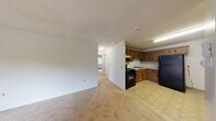 This single-floor unit offers a practical and straightforward layout designed for comfortable everyday living. The open-concept living area flows directly into the kitchen, creating a connected and functional common space. The living room is finished with neutral wall-to-wall carpeting and features a sliding glass door that opens to a private balcony, allowing natural light to fill the room and providing outdoor views of surrounding greenery.

The kitchen is positioned adjacent to the living area and is equipped with warm-toned wood cabinetry featuring decorative hardware, light countertops, a stainless steel sink, a black gas range with overhead ventilation, and a full-size black refrigerator. Tile flooring and a tiled backsplash complete the kitchen's functional aesthetic.

A hallway connects the living space to the private rooms, each carpeted and finished with neutral paint. The bedrooms each feature windows that bring in natural light and views of the surrounding neighborhood. Baseboard heating units run along the perimeter walls throughout the unit, providing consistent climate control. Textured ceilings are consistent throughout, contributing to the unit's understated, no-frills character.