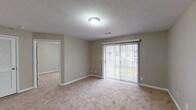 This single-floor unit offers a practical and comfortable layout designed to maximize its footprint. The living area is carpeted in a warm beige tone and features neutral taupe walls, white trim, and a sliding glass door fitted with vertical blinds that allows natural light to fill the space while providing access to an outdoor area. The front entry opens directly into the living space, which flows seamlessly toward the kitchen via dark wood-look vinyl flooring.

The galley-style kitchen is efficiently organized with warm wood cabinetry lining both sides, offering generous storage above and below the countertops. White appliances include a range with coil burners, a refrigerator, and a dishwasher, along with a built-in sink and range hood.

The bedroom is a well-sized carpeted room with a window dressed in vertical blinds, providing natural light and outdoor views. A louvered closet door offers convenient storage, and the room connects directly to the full bathroom. The bathroom features warm wood vanity cabinetry, a white countertop sink, and dark wood-look vinyl flooring, complementing the unit's consistent design aesthetic throughout.