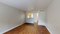 This two-floor space offers a practical and functional layout with a clean, neutral aesthetic throughout. The main living area is generously sized, finished with rich, dark hardwood-style flooring that extends across the open floor plan. Neutral gray walls and white trim create a bright, understated backdrop, while floor-mounted vents indicate a central HVAC system. A pass-through opening connects the living area to the kitchen, which features warm wood cabinetry, granite-look countertops, a double stainless steel sink, and a window that allows natural light and outdoor views into the space. A dishwasher is also present in the kitchen.

A separate entry area includes a front door with an adjacent window, bringing additional natural light into the home. The bedroom is carpeted and offers a ceiling fan with lighting, along with a window framing views of mature trees. The full bathroom is equipped with a tub-shower combo, toilet, wood vanity, granite-look countertop, and a large mirror with overhead lighting.

The lower level consists of an unfinished basement with a painted concrete floor and exposed ceiling joists, housing the water heater and furnace — providing functional utility space with potential for additional use.
