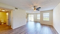 This single-floor unit offers a practical and comfortable layout across a thoughtfully organized floor plan. The combined kitchen and living room serves as the heart of the space, featuring durable wood-style flooring, warm neutral walls, and a textured ceiling with a ceiling fan fitted with a light fixture. Multiple windows, including a large sliding glass door, flood the living area with natural light and provide views of the surrounding greenery outdoors. The kitchen is equipped with light maple cabinetry, dark granite-style countertops, a decorative tile backsplash, and black appliances including a refrigerator, range, and over-the-range microwave. A louvered door in the kitchen leads conveniently to the laundry area. The bedroom is a generously sized, carpeted retreat featuring its own ceiling fan with light, a window with natural light, and direct access to adjacent rooms via a hallway. A dedicated closet provides ample storage. The entrance and hallway connect the rooms in a logical flow, contributing to the unit's overall efficiency. Throughout the space, consistent finishes and neutral tones create a clean, cohesive ambiance well-suited for comfortable everyday living.