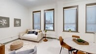 This 400 square foot studio apartment in Fort Wayne, Indiana, offers a thoughtfully designed living space that maximizes efficiency and style. The single-floor layout comprises a bright, open-plan living area, a modern kitchen, a well-appointed bathroom, and a closet for storage.

The living area is bathed in natural light from three large windows with wooden frames and horizontal blinds, offering views of the surrounding area. A comfortable white sofa serves as both seating and potential sleeping space, complemented by a small round side table. The room's neutral color palette, featuring white walls and light carpeting, creates an airy ambiance.

The kitchen boasts a sleek, contemporary design with white cabinetry and stainless steel appliances. It includes a full-sized refrigerator, built-in microwave, and a standard range, making it well-equipped for daily cooking needs. A round dining table with wooden chairs provides an eat-in area that transitions smoothly from the kitchen to the living space.

The bathroom is a standout feature, showcasing luxurious marble tiling in the shower area. It includes a bathtub-shower combination with chrome fixtures and built-in shelving for toiletries. The overall design of the apartment emphasizes clean lines and a minimalist aesthetic, creating a sense of spaciousness within the compact 400 square feet. This studio offers a perfect blend of functionality and modern style for urban living in Fort Wayne.