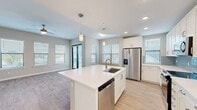 Located in Bonita Springs, FL, this well-appointed two-bedroom, two-bathroom unit offers a thoughtfully designed single-floor layout that maximizes both comfort and functionality. The heart of the home is an open-concept living, dining, and kitchen area filled with natural light from multiple windows. The kitchen is a standout, featuring a large central island with an undermount sink, crisp white cabinetry, a light blue subway tile backsplash, stainless steel appliances including a French door refrigerator, built-in microwave, and range, plus pendant lighting that adds a modern touch. Light wood-style flooring flows throughout the main living areas, complemented by ceiling fans for year-round comfort. Both bedrooms are carpeted and generously sized, each with natural light filtering through slatted blinds. The two bathrooms are finished with white vanity cabinetry, quartz-style countertops, and wood-look tile flooring, with one featuring a tub-shower combination. Three closets provide excellent storage, including a walk-in closet with wire shelving. A dedicated laundry room houses a full-size top-load washer and dryer. A private patio extends the living space outdoors, ideal for enjoying Florida's warm climate.