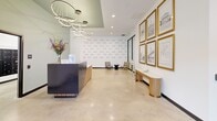 Located at 1314 Spring Garden St in Philadelphia's vibrant Spring Garden neighborhood, this amenity floor offers a thoughtfully designed, single-level space that serves as a welcoming hub for residents. The lobby makes a striking first impression with polished concrete floors, a sculptural multi-ring chandelier, and a sleek reception desk combining dark metal and warm wood slat detailing. A textured accent wall, patterned lounge chairs, and a curated gallery of gold-framed Philadelphia architectural prints add a distinctly local character to the space. Frosted glass partitions divide the lobby from a private office or meeting room, maintaining an open yet functional layout. Adjacent to the lobby, a dedicated mailroom houses an extensive array of built-in mailboxes, cleanly integrated into the white walls with polished concrete flooring underfoot. The fitness center is expansive and well-appointed, featuring rubber flooring, high ceilings with exposed ductwork painted in deep navy, and floor-to-ceiling windows that flood the space with natural light and offer views of the surrounding Philadelphia streetscape. Equipment includes treadmills, rowing machines, stationary bikes, cable machines, a power rack, TRX suspension systems, a dumbbell rack, and wall-mounted mirrors throughout. The overall aesthetic is contemporary and cohesive, balancing industrial elements with refined finishes.