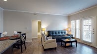 This single-floor residence offers a thoughtfully designed layout that balances comfort and functionality throughout its interconnected living spaces. Dark hardwood-style flooring flows consistently through the home, complemented by neutral-toned walls and crisp white baseboards that create a clean, cohesive aesthetic.

The living room features crown molding, natural light from large windows with plantation-style blinds, and direct access to an outdoor balcony. An adjacent dining area accommodates a round table with seating for four beneath additional crown molding details. The kitchen is equipped with dark cabinetry, granite countertops, stainless steel appliances, and a dedicated in-unit laundry closet nearby.

Both bedrooms are generously proportioned, each with ceiling fans, large windows allowing ample natural light, and dark wood furniture. The primary bedroom includes a walk-in closet with built-in shelving. Both bathrooms feature matching dark vanity cabinetry, granite countertops, subway-tiled shower-tub combinations with decorative mosaic tile accents, wood-look flooring, and dark-framed mirrors, delivering a consistent and refined finish throughout.