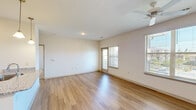 Located in Charlotte, NC, this one-bedroom, one-bathroom unit offers a well-designed layout that maximizes its comfortable footprint. The open-concept kitchen and living area serves as the heart of the home, featuring warm hardwood-style flooring throughout. The kitchen is appointed with rich wood cabinetry, granite countertops, a stainless steel appliance suite including a refrigerator, range, microwave, and dishwasher, and pendant lighting above the peninsula, which also doubles as a breakfast bar. The living area is bright and airy, with multiple windows dressed in blinds that invite natural light, complemented by a ceiling fan overhead. A sliding glass door provides access to an outdoor balcony area. The bedroom offers plush carpeting, a ceiling fan with light fixture, a dedicated closet, and a window with outdoor views. The full bathroom includes wood-style flooring, a tub/shower combination, and clean, neutral finishes. A dedicated laundry room houses a full-size washer and dryer alongside wire shelving for additional storage. The unit's neutral color palette and consistent finishes throughout create a cohesive and move-in-ready living environment.