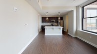 This well-designed single-floor residence combines modern finishes with a functional layout, creating a cohesive and inviting living environment. Rich, dark hardwood flooring flows consistently throughout the space, anchoring each room with warmth and style.

The open-concept kitchen is a standout feature, showcasing dark espresso cabinetry that extends to the ceiling, a mosaic tile backsplash, light quartz countertops, and a full suite of stainless steel appliances including a refrigerator with ice maker, electric range, and over-the-range microwave. A central island with pendant lighting above provides additional prep space and casual seating, seamlessly connecting the kitchen to the living area.

The spacious living room is highlighted by large windows that frame impressive city views, including notable urban architecture, and a sleek wall-mounted fireplace that serves as a refined focal point. The bright, neutral-toned walls complement the natural light that fills the room.

The bedroom is a calm, private retreat with clean lines, neutral walls, and direct access to an adjoining room. The bathrooms are tastefully appointed, featuring dark vanity cabinetry with white countertops, large mirrors, and modern fixtures. One bathroom includes a glass-enclosed walk-in shower with tile surround, while another offers a full vanity with ample storage.