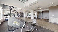 Located at 1184 Hank Aaron Dr in Atlanta, GA, this FitVibs fitness center offers a generously sized, open-plan workout space designed to accommodate a wide range of exercise routines. The facility spans a single floor and is thoughtfully organized into distinct training zones, providing ample room for both cardio and strength training activities.

The cardio area is outfitted with multiple treadmills and stationary bikes, all positioned along a bank of large windows that allow abundant natural light to fill the space and offer views of the surrounding Atlanta cityscape. Full-length mirrored walls further enhance the sense of openness and allow members to monitor their form during workouts.

The strength training section includes a dedicated stair-climbing machine, weight benches, dumbbells, and barbell equipment, giving members a comprehensive set of tools for resistance training. Structural columns define the zones without interrupting the overall flow of the space.

Throughout the facility, speckled rubber flooring provides both durability and comfort underfoot, while multiple ceiling fans ensure consistent air circulation. The clean, modern interior is characterized by a neutral white and gray color palette, accented by colorful artwork that adds a touch of personality. The overall ambiance is bright, functional, and welcoming, creating an environment well-suited for focused, effective training sessions.