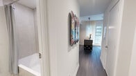 Located in Toronto's vibrant Liberty Village neighbourhood, this well-appointed one-bedroom, one-bathroom unit at 70 Ordnance Street offers a thoughtfully designed layout across a single floor. The open-concept kitchen and living area forms the heart of the home, featuring a sleek, contemporary kitchen with dark wood cabinetry, stainless steel integrated appliances, an induction cooktop, and a generous stone-topped breakfast bar with seating — ideal for both casual dining and entertaining. Under-cabinet linear lighting adds a refined finishing touch. The living area is bathed in natural light through floor-to-ceiling windows dressed with sheer curtains, offering views of the surrounding cityscape. Dark hardwood flooring flows throughout, grounding the bright, neutral palette. The bedroom is a serene retreat, comfortably sized with large windows overlooking the city skyline, a closet, and clean white walls that lend a calm ambiance. The full bathroom features a soaker tub with tiled surround, a dark wood vanity with stone countertop, and wood-look tile flooring, creating a cohesive, modern aesthetic. An entry hallway completes the functional layout of this refined urban residence.