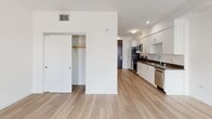 Located along the iconic Wilshire Boulevard in Los Angeles, this modern unit offers a thoughtfully designed single-floor layout with a clean, minimalist aesthetic. Light wood-tone flooring flows seamlessly throughout the open-concept living and kitchen areas, creating a cohesive and airy feel.

The kitchen is well-appointed with crisp white cabinetry, dark countertops, and a full suite of stainless steel appliances, including a range, built-in microwave, refrigerator, and dishwasher. Recessed lighting and ample cabinetry provide both functionality and style.

The living area is bright and open, benefiting from natural light that streams in through sliding glass doors leading to a private balcony. The balcony offers elevated views of the surrounding Los Angeles cityscape, adding an appealing outdoor element to the space. A dedicated closet with a hanging rod provides convenient built-in storage.

The bathroom features a full soaking tub with a shower, accented by floor-to-ceiling white subway tile that lends a clean, modern finish. The overall design of the unit prioritizes an open, uncluttered layout with white walls and contemporary finishes, resulting in a bright and inviting urban living space in the heart of Los Angeles.