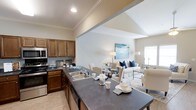 Located at 28013 Hwy 181 in Daphne, Alabama, this single-floor residence offers a thoughtfully designed open-concept layout that seamlessly connects the kitchen, dining, and living areas into one cohesive and functional space. The kitchen is well-appointed with warm wood cabinetry, dark countertops, stainless steel appliances including a built-in microwave and dishwasher, and a generous peninsula with an integrated sink — ideal for both meal preparation and casual dining. Crown molding accents the ceilings throughout, adding a refined architectural touch to the interior. The vaulted ceiling above the living area creates an elevated sense of openness, allowing the space to feel airy and expansive. The dining and living areas are bathed in natural light from nearby windows, enhancing the warm, welcoming ambiance. Light hardwood-style flooring runs throughout, complementing the neutral color palette of the walls and furnishings. The living area provides ample room for comfortable seating arrangements, making it well-suited for both everyday living and entertaining. Overall, this space combines practical design with tasteful finishes to create a comfortable and inviting single-floor home.