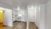 This single-floor unit offers a bright, efficient layout designed for comfortable everyday living. The open living area is finished with warm wood-tone laminate flooring that runs consistently throughout the space, creating a cohesive and welcoming atmosphere. A large window allows natural light to fill the room, complemented by a baseboard heating unit positioned beneath it.

The kitchen is thoughtfully designed with an L-shaped configuration, featuring crisp white cabinetry both above and below the countertops, a stainless steel sink, light-toned counters, and a full suite of white appliances including a gas range and a full-size refrigerator. Under-cabinet lighting adds functional brightness to the workspace. The entry door is conveniently located adjacent to the kitchen, with a louvered closet door nearby providing additional storage at the entryway.

The bedroom is a well-proportioned room with clean white walls and the same laminate flooring, anchored by a set of wide sliding panel doors that open to a generously sized closet — a standout storage feature of the space.

The bathroom is neatly appointed with a white tiled tub-shower combination, brushed nickel fixtures and hardware, a toilet, and a vanity with storage below. The overall aesthetic throughout the unit is clean, minimal, and move-in ready.
