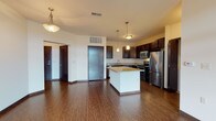 This single-floor residence at 20905 Villa Ct in Waukesha, Wisconsin offers a thoughtfully designed open-concept layout with consistent, modern finishes throughout. The kitchen serves as a central highlight, featuring dark espresso cabinetry, granite countertops, a central island with additional granite surface space, and a full suite of stainless steel appliances including a refrigerator, range, microwave, and dishwasher. Pendant lighting above the island and additional overhead fixtures provide warm, layered illumination. Rich hardwood-style flooring extends throughout the kitchen and main living area, creating a cohesive and polished aesthetic. The generously sized living area benefits from access to an outdoor space through a glass door, allowing natural light to fill the room. The bedroom features plush carpeting, tall windows that invite substantial natural light, and views of the surrounding building community. The bathrooms are finished with dark cabinetry, stone-topped vanities, brushed nickel hardware, and light tile flooring. One bathroom includes a full tub-shower combination. The overall ambiance is clean, contemporary, and move-in ready.