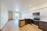 Located at 3118 6th Avenue in Tacoma, WA, this 2-bedroom, 1-bathroom unit offers a thoughtfully designed open-concept layout with light wood-style flooring throughout. The kitchen serves as a functional centerpiece, featuring dark lower cabinetry paired with white upper cabinets, a clean tile backsplash, white quartz countertops, and a full suite of stainless steel appliances including a refrigerator, electric range, microwave, and dishwasher. A peninsula with a sink provides additional prep space and separates the kitchen from the living area. The living room is bright and airy, with clean white walls and a sliding glass door that opens to a private balcony overlooking the surrounding neighborhood. The primary bedroom is a comfortable size and includes a closet with wire shelving for organized storage. The bathroom is well-appointed with a wide vanity, dark wood cabinetry, a large mirror, and light wood flooring that ties seamlessly into the rest of the unit. A dedicated closet near the entry adds convenient storage. The overall design aesthetic is clean and contemporary, with a neutral palette and modern finishes that create a cohesive, move-in-ready living space.