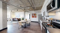 Located at 708 22nd Street in Greeley, CO, this thoughtfully designed one-bedroom, two-bathroom unit delivers a striking urban aesthetic across a single floor. The open-concept living, dining, and kitchen area immediately impresses with its signature exposed concrete ceiling, visible conduit, and track lighting — hallmarks of industrial-modern design — all anchored by warm hardwood-style flooring throughout.

The kitchen is well-appointed with white shaker cabinetry, stainless steel appliances including a refrigerator, range, microwave, and dishwasher, and a dark stone countertop. It flows seamlessly into the dining area and spacious living room, which benefits from a large window that fills the space with natural light and offers outdoor views.

A dedicated office provides a quiet retreat, featuring carpet underfoot, a wide window overlooking a balcony and tree-lined surroundings, and ample room for a functional workspace.

The bedroom is a comfortable sanctuary with plush carpet, a generous closet with a bold black-framed door, and natural light streaming through a window with outdoor views. Both bathrooms are clean and modern, with one featuring a full soaking tub surrounded by crisp white tile. The hallway entry, accented by exposed concrete ceilings and contemporary art, ties the aesthetic of the entire unit together.