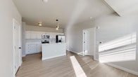 This contemporary single-floor unit offers a thoughtfully designed open-concept layout that seamlessly connects the kitchen and living areas. The kitchen serves as the centerpiece of the space, featuring a large central island with a light quartz countertop and an undermount stainless steel sink, accented by a sleek pendant light overhead. White shaker-style cabinetry lines the perimeter walls, paired with a full suite of stainless steel appliances including an electric range, over-the-range microwave, and a French door refrigerator with an in-door ice and water dispenser. Light hardwood-style flooring extends throughout, lending warmth and visual continuity to every room. The living area is bathed in natural light from multiple windows, creating a bright and welcoming ambiance. The clean, neutral color palette of white and soft grey tones enhances the sense of openness throughout. The bathrooms maintain the same modern aesthetic, with white shaker vanity cabinetry, quartz countertops, large wall mirrors, and wood-look tile flooring. A full tub-shower combo is featured in one bathroom, while a dedicated vanity area with ample cabinet storage is found in another. Overall, the space presents a clean, move-in-ready interior with cohesive modern finishes.