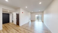 Located in Bozeman, MT, this one-bedroom, one-bathroom residence at University Crossing offers a clean, contemporary design throughout. Light-toned luxury vinyl plank flooring runs continuously across the entire floor plan, complementing the crisp white walls and recessed lighting that keep the space feeling bright and open.

The combined kitchen and living area forms the heart of the unit. The kitchen is outfitted with two-tone cabinetry — slate-blue lower cabinets paired with light wood-grain uppers — white quartz countertops, a stainless steel sink, and a full suite of stainless steel appliances including a range, over-the-range microwave, refrigerator, and dishwasher. The living area flows naturally from the kitchen and opens to a private balcony through sliding glass doors, allowing natural light to fill the space and providing views of the surrounding Bozeman landscape.

The bedroom features warm gray accent walls, a generous window with outdoor views, and dedicated closet storage. The full bathroom includes a soaking tub with tiled surround, a wide vanity with an undermount sink and white countertop, and a large mirror. A dedicated laundry room houses a stacked full-size washer and dryer with additional cabinetry and counter space. An entry hallway with wall hooks completes this efficiently designed, move-in-ready residence.