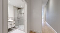 This thoughtfully designed single-floor unit offers an efficient yet stylish layout encompassing an open-concept living, dining, and kitchen area, one full bathroom, and a dedicated closet. Light hardwood flooring flows throughout, lending warmth and visual continuity to the space.

The main living area is anchored by a large window that frames urban views, filling the room with natural light. Exposed ductwork near the ceiling adds an industrial character, complementing the otherwise clean, contemporary aesthetic. The kitchen is well-appointed with white shaker-style cabinetry featuring glass upper panels, a marble-effect tile backsplash, white quartz countertops, and a full suite of stainless steel appliances. The adjoining dining area comfortably accommodates a round table and seating, with a gallery wall adding a curated artistic touch.

The bathroom is finished to a high standard, featuring a floating white vanity with an undermount sink, warm-toned hardware accents, a large backlit mirror, and a glass-enclosed walk-in shower clad in neutral grey tile. A hallway with recessed lighting connects the living spaces to the bathroom and closet, maintaining a clean and uncluttered flow throughout the unit. The overall ambiance is modern, bright, and refined.