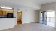 This 1-bedroom, 1-bathroom residence is thoughtfully laid out across a single floor, offering a practical and comfortable living environment. The living area serves as the heart of the unit, featuring plush wall-to-wall carpeting, clean white walls, and a textured ceiling that adds subtle character. Vaulted or elevated ceiling lines lend a sense of openness to the space, making it feel more expansive than its footprint might suggest. A sliding glass door opens directly to a private balcony, filling the living area with natural light and providing a pleasant outdoor retreat with wooded views. Adjacent to the living room, the kitchen is equipped with wood-toned cabinetry and dark appliances, including a refrigerator, and features a breakfast bar that creates a casual dining option. The entryway, finished with hardwood-style flooring, provides a clean transition into the living space and includes a dedicated HVAC unit. Central air distribution vents are present throughout, ensuring year-round climate comfort. The overall ambiance is clean, neutral, and move-in ready, with a straightforward design that makes the space highly functional and easy to personalize.