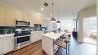 Located at 2074 Fox Valley Center in Aurora, IL, this single-floor residence offers a thoughtfully designed open-concept layout that seamlessly connects the kitchen, dining, and living areas. The kitchen is a standout feature, showcasing crisp white cabinetry extending to the ceiling, a striking blue subway tile backsplash, stainless steel appliances including a gas range and built-in microwave, and a generous island with a white quartz countertop illuminated by paired brushed-gold pendant lights. Rich hardwood-style flooring runs throughout the main living areas, adding warmth and continuity. The living room is bathed in natural light from large windows and provides ample space for comfortable seating and dining, with clean white walls that enhance the bright, airy atmosphere. The bedroom offers a serene retreat with plush carpeting and soft natural light. The bathroom includes a glass-enclosed shower and leads directly to a walk-in closet, offering practical convenience. Throughout the space, the design maintains a consistent modern aesthetic with neutral tones, quality finishes, and functional layouts that balance everyday livability with contemporary style.