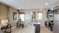 This single-floor 1-bedroom, 1-bathroom residence offers a well-designed open-concept layout that seamlessly connects the kitchen and dining areas, creating a functional and inviting living environment. The kitchen is a standout feature, showcasing a sleek island with a light granite countertop, an undermount sink, and pendant lighting that adds a polished, modern touch. Dark cabinetry provides a striking contrast against the lighter surfaces, contributing to a contemporary aesthetic. The dining area is efficiently arranged with a bistro-style high table and matching stools, positioned near a glass-paneled door that invites natural light into the space. Multiple windows dressed with patterned fabric valances and white blinds allow for ample daylight while maintaining privacy. Light wood-toned flooring runs throughout, enhancing the sense of openness and warmth. Neutral warm-beige walls serve as a versatile backdrop, complemented by tasteful wall art and decorative accents. Recessed ceiling lighting ensures the space remains bright and well-lit throughout the day. Overall, this residence combines practical design with modern finishes to deliver a comfortable and stylish single-floor living experience.