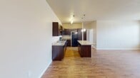 Located at 13331 N MacArthur Blvd in Oklahoma City, Oklahoma, this single-floor unit offers a well-designed, open-concept layout with a cohesive blend of style and practicality throughout. The expansive living area features warm hardwood-style flooring, a ceiling fan with light fixture, and large windows fitted with horizontal blinds that invite abundant natural light and offer views of the surrounding neighborhood. The kitchen is a standout feature, showcasing rich dark espresso cabinetry, granite countertops, a central island with pendant lighting overhead, a track lighting system, and a full suite of black appliances including a range, microwave, dishwasher, and refrigerator — all set atop continuous hardwood-style flooring. The bedrooms are comfortably carpeted and include ceiling fans, with windows providing additional natural light. The bathrooms are finished with dark wood vanities, contrasting countertops, hardwood-style flooring, and well-lit mirrors. One bathroom features a full tub-shower combination. A dedicated laundry room includes a full-size washer and dryer with overhead shelving for added storage convenience. Neutral tones and clean white trim carry throughout the unit, creating a bright and cohesive atmosphere from room to room.