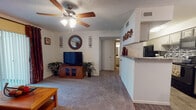 This single-floor residence is thoughtfully designed to maximize functionality across its living spaces. The living room serves as the central hub of the home, featuring soft wall-to-wall carpeting, a ceiling fan with integrated lighting, and a textured ceiling. A half-wall partition seamlessly connects the living area to the kitchen, creating an open feel while maintaining a defined layout. The front entry area transitions from tile flooring into the carpeted living space, providing a natural boundary at the door.

The kitchen is well-appointed with cream cabinetry, granite-style countertops, and a striking mosaic tile backsplash in neutral tones. Black appliances, including a refrigerator, electric range, and over-the-range microwave, provide a cohesive, modern contrast to the lighter cabinetry. Wood-look flooring runs throughout the kitchen, adding warmth and practicality.

The bedroom is a comfortable retreat featuring plush carpeting, a ceiling fan, and a window that allows natural light to filter through. A textured ceiling carries throughout the space consistently.

The bathroom is efficiently laid out with wood-look flooring, a tub and shower combination with tile surround, and clean white fixtures. Each room reflects a cohesive, neutral color palette throughout.
