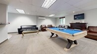 Located at 520 Mornington Ave in London, Ontario, this single-floor amenity space serves as a well-designed recreation and social hub. The open-concept layout is divided into distinct functional zones that flow seamlessly into one another, creating a versatile and inviting environment.

At the heart of the space sits a striking pool table with a bold blue felt surface and a distinctive natural wood and black metal frame, making it both a functional centerpiece and a visual focal point. Surrounding it is a generously sized lounge area furnished with leather sofas and armchairs, complemented by a glass-top coffee table — ideal for relaxed social gatherings. A wall-mounted mini-split system ensures year-round climate comfort, while a window brings in natural light and outdoor views.

Adjacent to the recreation area, a kitchenette features white cabinetry with dark countertops and tile flooring, providing practical amenities for entertaining or casual use. Track lighting and recessed panel ceiling lights illuminate the space evenly throughout.

The interior is finished with neutral-toned carpet in the lounge and game areas, transitioning to smooth tile near the kitchenette and entry. Mirrored sliding doors and clean white walls contribute to a bright, modern aesthetic. Framed artwork accents the walls, adding a polished, curated touch to this thoughtfully designed communal space.
