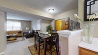 This single-floor, 3-bedroom, 1-bathroom residence offers a thoughtfully arranged layout that maximizes functionality across its living spaces. The carpeted living room provides a welcoming atmosphere, featuring a large window dressed with sheer white curtains that allow natural light to fill the room, complemented by neutral warm-toned walls throughout.

The dining area is positioned adjacent to the living room and is defined by a half-wall partition with built-in shelving, offering both separation and an open feel. The space comfortably accommodates a full dining set and features a bold piece of wall art that adds visual interest.

The kitchen is equipped with warm oak cabinetry, white tile backsplash, a stainless steel sink, electric range, and dishwasher, with tile flooring and windows providing natural light. A separate door in the kitchen leads to an exterior entry point.

The primary bedroom offers a comfortable footprint with carpeted flooring, a window with sheer curtains, and a closet with a full-length hanging rod and built-in shelf for storage. The additional bedrooms follow a similar design aesthetic with neutral walls and carpet.

The bathroom includes a single-sink vanity with oak cabinetry, a tub-shower combination, tile flooring, and tasteful finishes. The overall design of the space is cohesive, with warm neutral tones and practical features throughout.