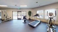 Located in Martinez, California, this single-level fitness center offers a comprehensive workout environment designed to accommodate a range of exercise needs. The space is organized to provide distinct areas for both cardiovascular and strength training activities, with durable rubber flooring throughout that is well-suited for high-traffic use.

The cardio section is equipped with multiple Spirit-brand machines, including treadmills, an elliptical, and a stationary bike, arranged to allow comfortable spacing between equipment. Large windows fitted with vertical blinds line the walls, allowing natural light to fill the space while maintaining privacy. A glass door provides direct exterior access, adding to the sense of openness and ventilation.

The strength training area features cable machines and a multi-function weight station, positioned alongside a full-length glass mirror wall that visually expands the room and allows users to monitor their form. Recessed fluorescent lighting supplements natural light, ensuring the space remains well-lit throughout the day.

Neutral-toned walls, decorative plants, and a clean, uncluttered layout contribute to a welcoming and functional atmosphere. The fitness center is thoughtfully appointed to serve a broad range of users seeking an accessible and practical exercise facility.