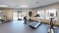 Located in Martinez, California, this single-level fitness center offers a comprehensive workout environment designed to accommodate a range of exercise needs. The space is organized to provide distinct areas for both cardiovascular and strength training activities, with durable rubber flooring throughout that is well-suited for high-traffic use.

The cardio section is equipped with multiple Spirit-brand machines, including treadmills, an elliptical, and a stationary bike, arranged to allow comfortable spacing between equipment. Large windows fitted with vertical blinds line the walls, allowing natural light to fill the space while maintaining privacy. A glass door provides direct exterior access, adding to the sense of openness and ventilation.

The strength training area features cable machines and a multi-function weight station, positioned alongside a full-length glass mirror wall that visually expands the room and allows users to monitor their form. Recessed fluorescent lighting supplements natural light, ensuring the space remains well-lit throughout the day.

Neutral-toned walls, decorative plants, and a clean, uncluttered layout contribute to a welcoming and functional atmosphere. The fitness center is thoughtfully appointed to serve a broad range of users seeking an accessible and practical exercise facility.