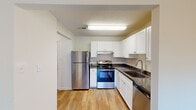 Located at Silver Lake Blvd in Alexandria, VA, this one-bedroom, one-bathroom residence offers a thoughtfully organized single-floor layout. The kitchen is a standout feature, equipped with stainless steel appliances including a full-size refrigerator, electric range, and dishwasher. Crisp white cabinetry provides ample storage, while dark granite-style countertops and a double-basin sink add a polished contrast. Light hardwood-style flooring runs throughout the kitchen, living areas, and hallway, lending a clean and cohesive aesthetic. The living room is bright and open, highlighted by a sliding glass door that opens to a private balcony overlooking lush, tree-lined surroundings, bringing in generous natural light. The bedroom is a comfortable, well-proportioned space with soft carpet flooring, a window with outdoor views, and neutral walls that create a calm retreat. The bathroom features hardwood-style flooring, a wood-toned vanity with storage, and accessibility-friendly grab bars. A hallway connects the rooms efficiently, completing the functional floor plan. Throughout the residence, textured ceilings and neutral tones create a consistent, understated ambiance well-suited for comfortable everyday living.