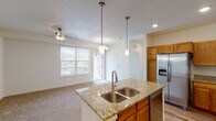 This single-floor residence offers a thoughtfully designed open layout that seamlessly connects the kitchen and living areas. The kitchen serves as the centerpiece of the home, showcasing a large granite-topped island with a double stainless steel sink and pendant lighting overhead. Warm-toned wood cabinetry lines the walls from floor to ceiling, complemented by a full suite of stainless steel appliances including a French door refrigerator with ice maker, electric range, over-the-range microwave, and dishwasher. The flooring transitions from durable wood-look planks in the kitchen to plush neutral carpet throughout the living and bedroom areas, creating a comfortable and cohesive feel. The bedrooms are bright and airy, each featuring windows with blinds that invite natural light and offer views of the surrounding neighborhood and landscaping. Ceiling fans add to the comfort of these spaces. The bathrooms are clean and functional, finished with wood cabinetry vanities topped with stone counters, wood-look flooring, and full tub-shower combinations with brushed nickel fixtures and large mirrors. The overall ambiance of the home is light, neutral, and move-in ready, with consistent finishes throughout that lend a polished, cohesive character to every room.