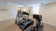 The Revere Village Fitness Center, located at 865 Revere Village Ct in Dayton, Ohio, is a dedicated single-floor exercise facility designed to support a well-rounded fitness routine. The space is identified by its branded glass entry door featuring the Revere Village Fitness Center logo, providing a welcoming and professional entry point.

The interior is finished with neutral yellow-toned walls, textured ceilings with recessed lighting, and wall-to-wall carpet flooring accented by rubber equipment mats. Natural light filters in through multiple windows fitted with blinds, contributing to a bright and motivating atmosphere.

The facility is equipped with a suite of premium Landice cardio machines, including treadmills, an elliptical trainer, and a recumbent exercise bike, all positioned throughout the open floor area. A multi-function strength training cable machine with an adjustable bench is available for resistance and weight training exercises. A wall-mounted television is present for entertainment during workouts.

Motivational wall decor, including the phrase "Everyday is a good day to work out," adds an encouraging atmosphere. Posted fitness center rules and exercise room guidelines are displayed for resident reference. The space also includes a restroom, ensuring convenience for users. The overall design is clean, functional, and well-maintained, making it a practical fitness resource for Revere Village residents.