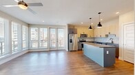 This thoughtfully designed 2-bedroom, 2-bathroom residence offers a comfortable and modern living experience across a single floor. The open-concept kitchen and living area serves as the heart of the home, anchored by a spacious kitchen island with a smooth gray countertop and stylish pendant lighting. The kitchen is outfitted with two-tone cabinetry — light wood upper cabinets paired with gray lower cabinets — a decorative tile backsplash, stainless steel appliances, and a black hardware finish throughout. Light wood-style flooring extends seamlessly across the main living area, complementing the bright, airy atmosphere created by large floor-to-ceiling windows and glass doors that invite plentiful natural light and outdoor views. Both bedrooms feature ceiling fans, plush carpeting, and windows with city views. The generously sized primary bedroom includes access to a walk-in closet with wire shelving systems for ample storage. Each bathroom is finished with modern wood-tone vanities, dark-framed mirrors, undermount sinks, and tile flooring. A well-connected hallway provides easy access to all rooms, completing this clean, contemporary floor plan designed for both comfort and functionality.