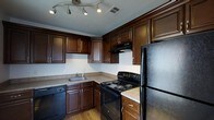 This single-story residence features two bedrooms and two bathrooms, offering a thoughtfully arranged floor plan that maximizes comfort and functionality. The kitchen stands out as a practical and attractive centerpiece, showcasing rich dark wood cabinetry with brushed nickel hardware that extends from floor to ceiling, providing substantial storage throughout. Granite-style countertops offer ample prep space, complementing the suite of black appliances that includes an electric range, dishwasher, and refrigerator. A built-in range hood adds both function and a clean, finished look. The kitchen is further enhanced by hardwood flooring and a track lighting system overhead, ensuring excellent illumination across the workspace. A stainless steel sink is conveniently positioned beneath upper cabinetry, adding to the room's efficient layout. The neutral wall tones throughout create a versatile backdrop that suits a variety of décor styles. With two full bathrooms and two well-sized bedrooms, this residence provides an ideal balance of private and shared living spaces, making it well-suited for individuals, couples, or roommates seeking a comfortable, move-in-ready home.