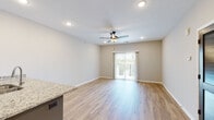 This single-story space in Grain Valley, Missouri, presents a thoughtfully designed open-concept layout with contemporary finishes throughout. Light wood-look flooring flows through the main living areas, complementing the neutral gray-toned walls and crisp white trim.

The kitchen serves as a functional centerpiece, featuring a peninsula with striking navy blue cabinetry paired with granite countertops, a stainless steel sink, and a full suite of stainless steel appliances including a refrigerator, range, and over-the-range microwave. White subway tile backsplash and gray upper cabinetry complete the polished look.

The living area is bright and open, with recessed lighting, a ceiling fan, and sliding glass doors that lead to a private balcony with outdoor views. A separate dining area flows naturally from the kitchen peninsula.

Bedrooms feature plush carpeting, ceiling fans, and windows with blinds that allow ample natural light. One bedroom includes a private en-suite bath with wood-look flooring. Bathrooms are finished with granite-topped vanities, gray shaker-style cabinetry, brushed nickel hardware, and large mirrors with modern light fixtures. A louvered storage closet and additional utility access add practical functionality to the space.