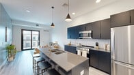 This contemporary 940 square foot apartment offers a harmonious blend of style and functionality. The open-concept layout maximizes the use of space, creating a seamless flow between the living areas. The kitchen is a standout feature, boasting sleek dark cabinetry, stainless steel appliances, and a generous island with seating, perfect for casual dining or entertaining.

The living room is bathed in natural light, thanks to large windows that offer city views. A modern white sofa, geometric wooden coffee table, and artistic wall decor create a sophisticated ambiance. The bedrooms, including a 150 square foot primary suite, feature comfortable beds, minimalist decor, and ample natural light.

Both bathrooms showcase clean lines with white fixtures, modern vanities, and stylish finishes. The apartment's cohesive design is evident in the consistent use of light wood flooring throughout, which complements the predominantly white walls and adds warmth to the space.

Additional features include built-in storage solutions, pendant lighting, and thoughtfully placed artwork. The apartment's layout efficiently accommodates four bedrooms without sacrificing living space, making it an ideal home for those seeking a balance of privacy and communal areas in an urban setting.