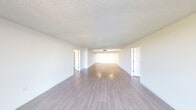 This single-floor residence offers a clean, contemporary layout designed to maximize space and natural light. The expansive main living area is immediately striking, featuring light hardwood-style flooring that runs continuously throughout the unit, crisp white walls, and a textured popcorn ceiling. Large sliding glass doors lead to a private balcony, flooding the interior with abundant natural light and offering views of the surrounding landscape and waterway.

The galley-style kitchen is thoughtfully designed with white shaker cabinetry, light stone countertops, stainless steel hardware, a stainless steel refrigerator, and a built-in sink — providing ample storage and counter space in an efficient layout.

The space includes two bathrooms. The primary bathroom features a wide vanity with a light stone countertop, a large mirror, and a full soaking tub with a shower combination. The secondary bathroom is equipped with a single vanity and a glass-enclosed standing shower. Both bathrooms are finished with hardwood-style flooring consistent with the rest of the unit.

Additional highlights include a spacious walk-in closet with built-in shelving, a dedicated storage area, and a bifold closet in the main living space. The unit's all-white palette and consistent flooring create a cohesive, move-in-ready environment throughout.