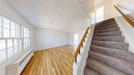 Located at 108 Kendall Ct in Dover, NJ, this two-story unit offers two bedrooms and one bathroom thoughtfully distributed across two floors. The main floor houses the living room and kitchen, while the upper floor contains both bedrooms and the bathroom, connected by a staircase with a classic wooden banister.

The living room welcomes natural light through double-hung windows and features warm hardwood flooring, white walls, and a radiator heating unit. A textured ceiling adds subtle character to the space. The kitchen is equipped with warm-toned oak cabinetry, dark countertops, a double sink, and white appliances including a range and refrigerator. Tile flooring, a pendant light fixture, and a windowed exterior door brighten the room considerably.

Upstairs, both bedrooms continue the hardwood flooring theme and are finished with clean white walls and natural light from multiple windows. The primary bedroom is a comfortable size with radiator heating. The full bathroom features classic black-and-white tile work, a white vanity, and a bathtub with shower, maintaining a clean, timeless aesthetic throughout.