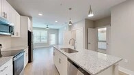 Located at 350 Bay Laurel Dr in Saint Augustine, FL, this thoughtfully designed one-bedroom, one-bathroom residence offers a clean, modern aesthetic throughout its efficiently utilized single-floor layout. The open-concept kitchen serves as the heart of the home, showcasing a granite-topped island with an undermount sink, sleek white shaker cabinetry, stainless steel appliances including a refrigerator, range, and microwave, and stylish pendant lighting. Light wood-look flooring flows through the main living and kitchen areas, creating a seamless, airy feel. The living area benefits from natural light through multiple windows with blinds and is finished with a ceiling fan for added comfort. The generously sized primary bedroom features plush carpeting, large windows, and a ceiling fan, offering a comfortable retreat. The bathroom is well-appointed with a granite vanity, white cabinetry, wood-look flooring, and a tiled shower-tub combination. A dedicated walk-in closet with wire shelving provides ample storage, while a separate in-unit laundry room with a full-size washer and dryer adds everyday convenience. The overall ambiance is bright, clean, and contemporary.